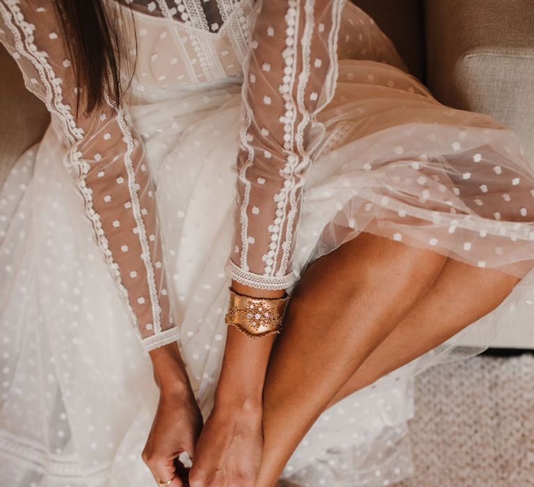 Bride in a polka dot tulle wedding dress putting on her gold strappy sandals 