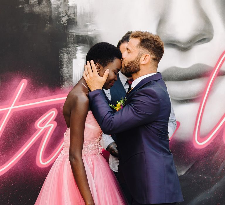 Groom kisses bride on the forehead as they stand in front of graffiti mural in Italy 