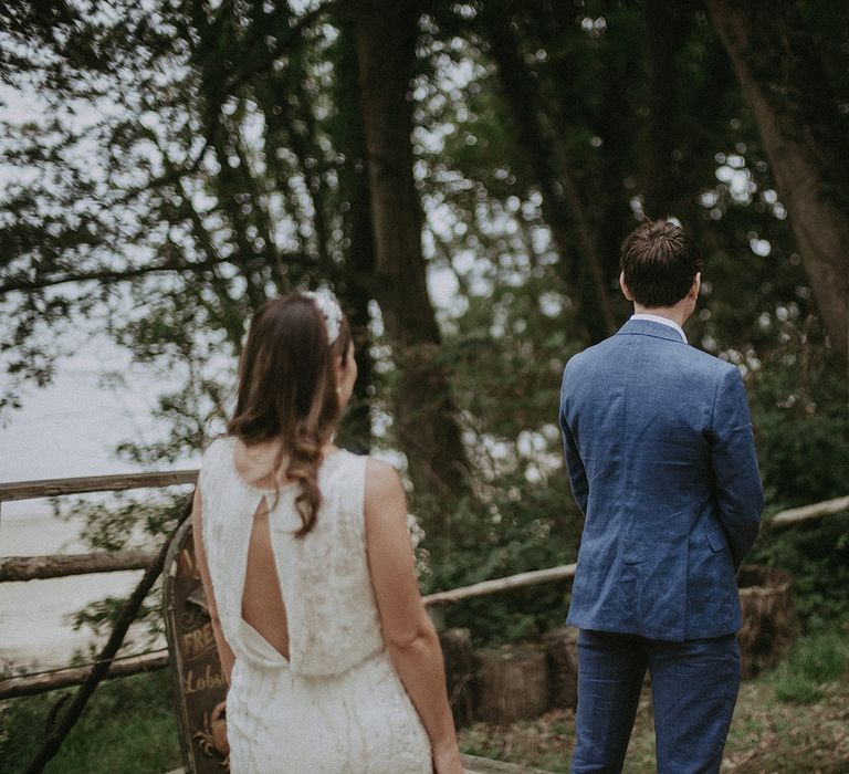 Bride stands behind groom as she waits for first look moment to be captured