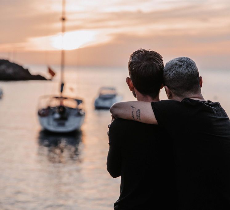 Grooms hold one another as they look out onto the sea