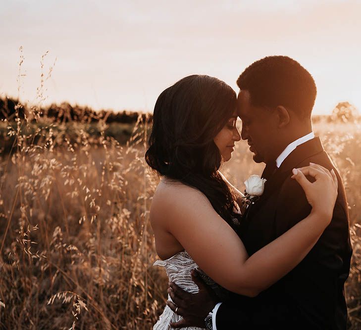 Golden hour portrait with bride and groom embracing in a field 