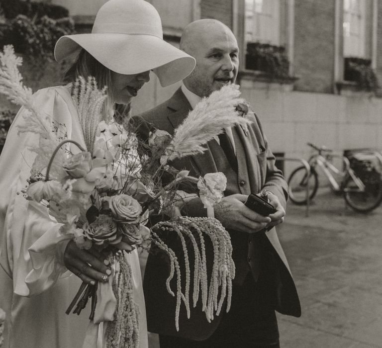 Bride & groom walk together through Chelsea as bride wears floppy wedding hat