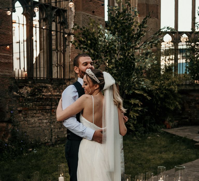 Groom embracing his bride in a bow veil surrounded by pillar candles at a bombed out church in Liverpool 