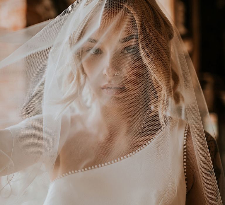 Bride in a one shoulder wedding dress with sheer veil over her face