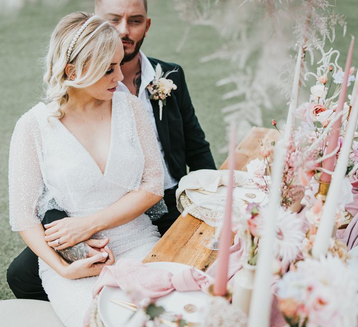 Bride in a sparkly wedding dress sitting at her pastel pink wedding reception table with her husband 