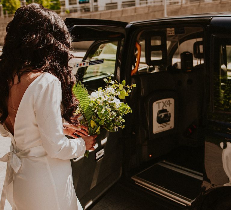 Bride in a Chi Chi London wedding dress with long sleeves and bow detail getting into a London black cab 