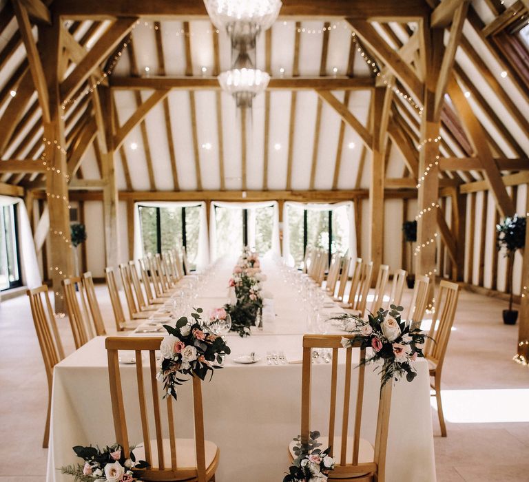 Pink and white roses and green floral decor on wooden chairs in wedding reception at Old Kent Barn 