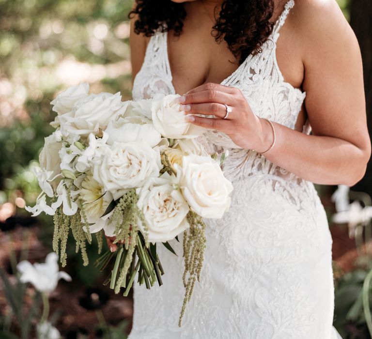 Black bride smiles and laughs as she wears strappy wedding gown whilst looking to her white classic floral bouquet