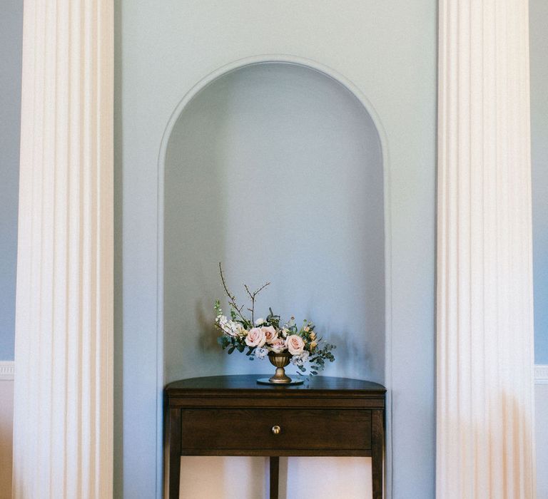 classic pink rose floral arrangement in a gold vessel sitting on a console table