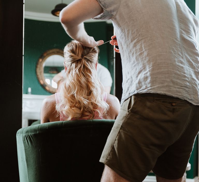 Bride has her hair done on the morning of her wedding as it is pulled back and curled