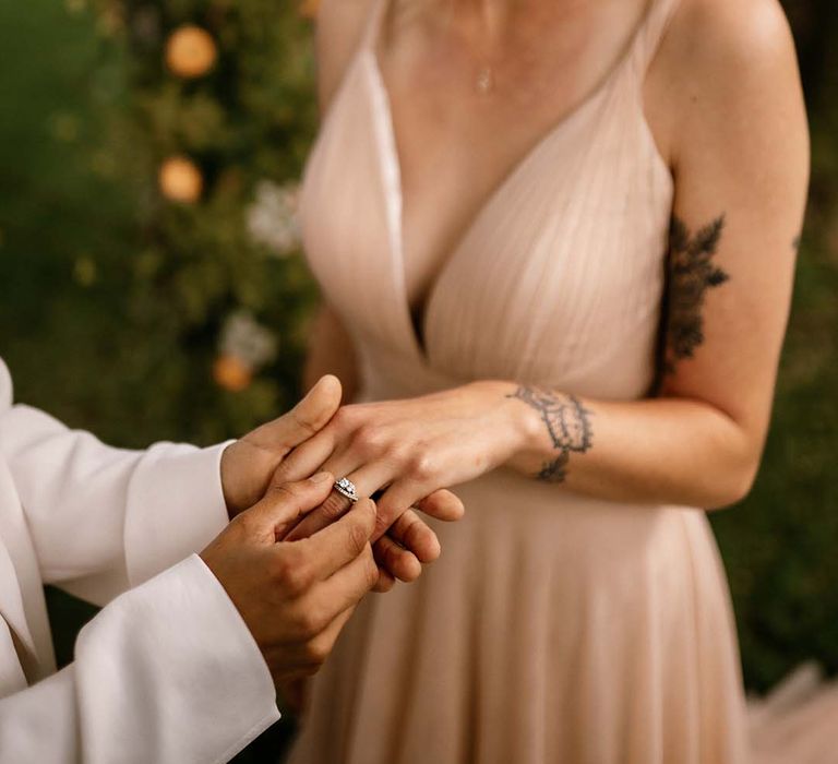 Bride putting a diamond wedding ring on her brides finger 