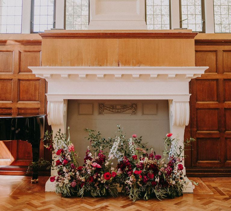 Fireplace at Dulwich College decorated in a low floral arrangement with deep red and pink wedding flowers and foliage 