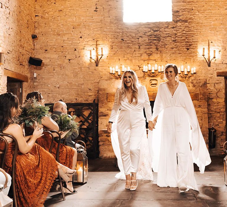 Brides hold hands and walk down the aisle with one another on their wedding day