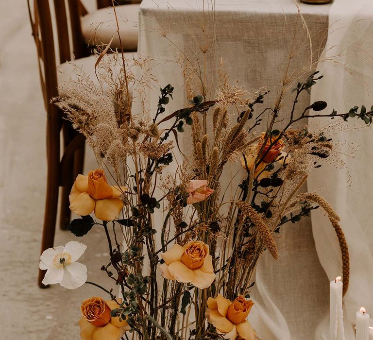 Fresh orange and yellow peeled back roses and dried grass low floral arrangement 