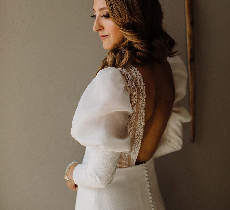 Bride wears bridal gown complete with low-cut back with lace trim and puff sleeves