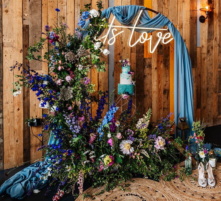 Confetti cone wall, neon sign and three-tier wedding cake surrounded by wildflower decor 