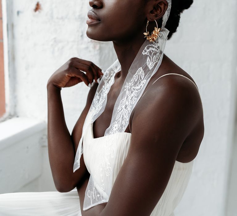 Black bride in a sweetheart neckline wedding dress with thin straps wearing a embroidered bow around her head 