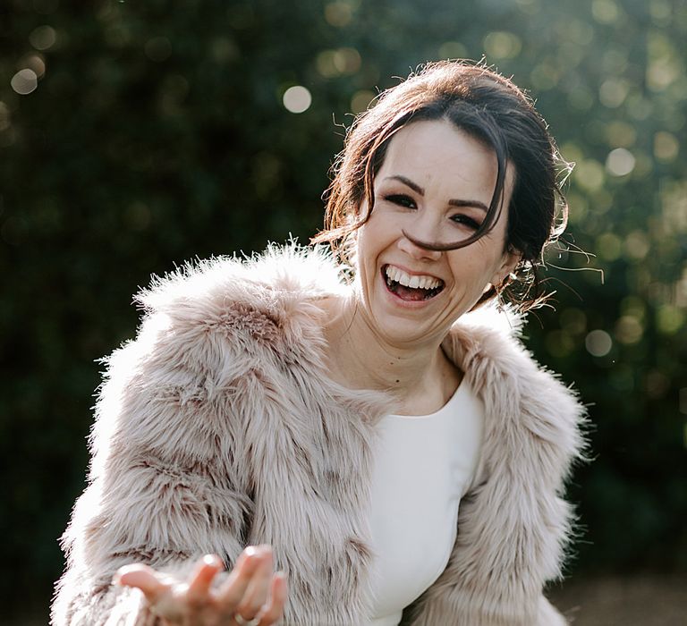 Bride in a fitted wedding dress in a biscuit coloured long faux fur coat for Winchester Registry Office wedding 