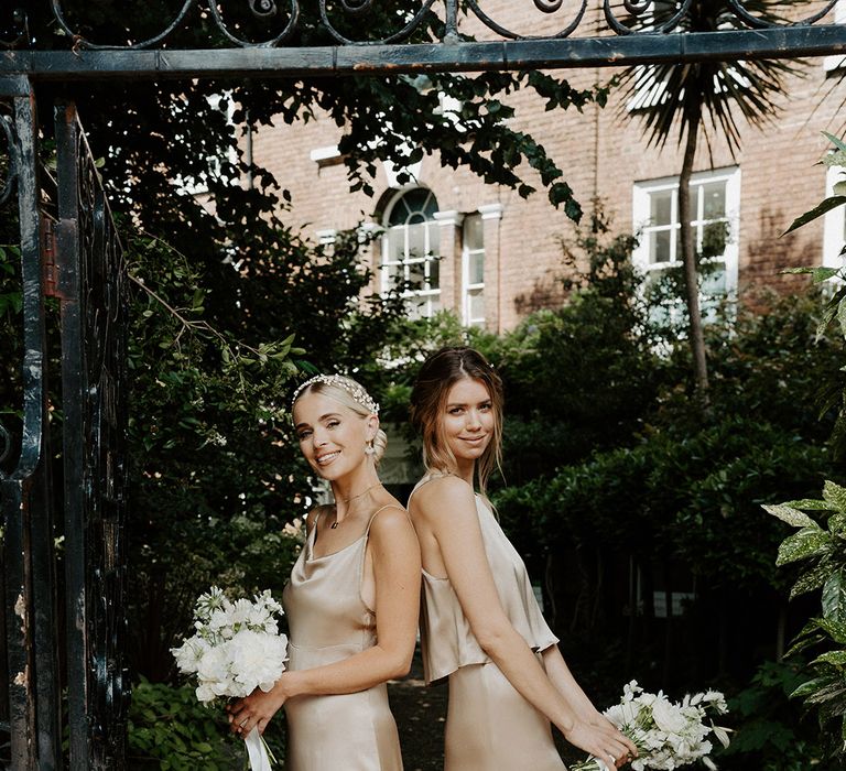 Bridesmaids in different gold satin bridesmaid dresses by Constellation Ame holding white bouquets 