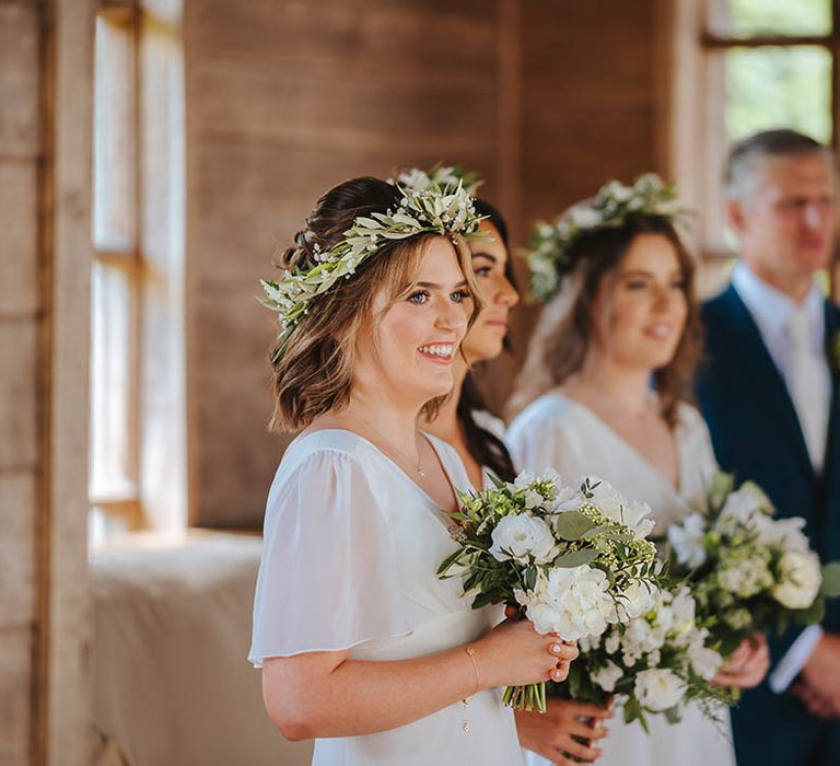 Bridesmaids look on during wedding ceremony whilst holding floral bouquets