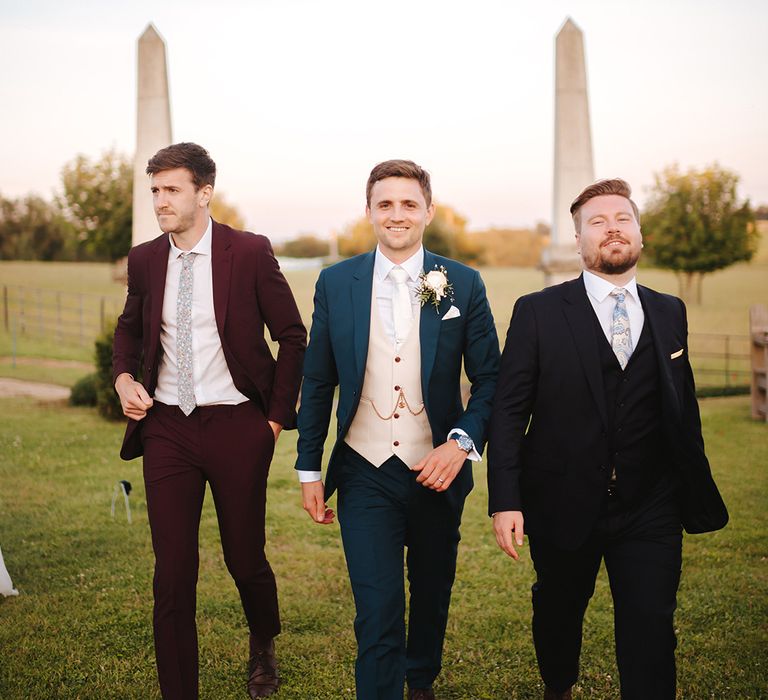 Groom & his groomsmen walk together across grass on wedding day