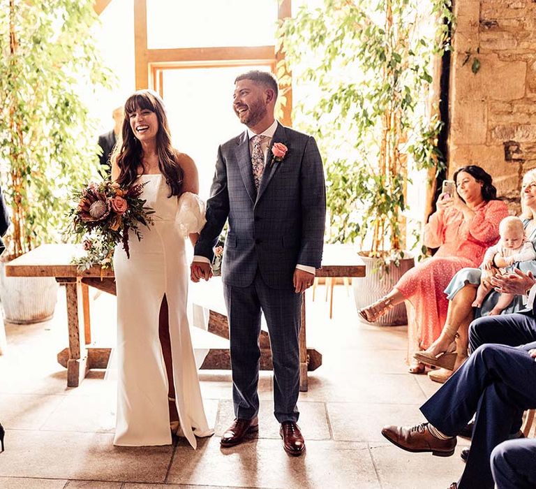 Bride & groom laugh as they hold hands with one another after wedding ceremony at the Stone Barn Cotswolds 