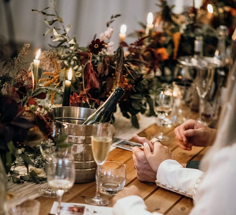 Bride holds her grooms hand on the day of her wedding as they sit at rustic table