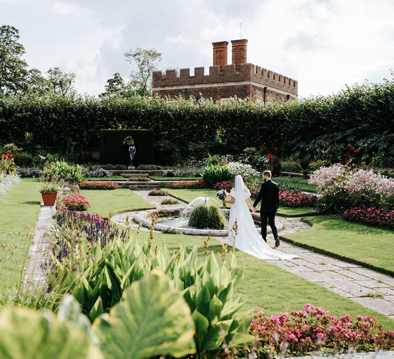 Bride & groom walk together through the gardens of Hampton Court Palace