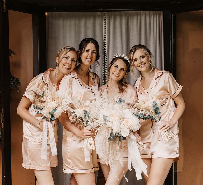 Bride stands with her bridesmaids on the morning of her wedding day as they all wear matching silk pyjamas