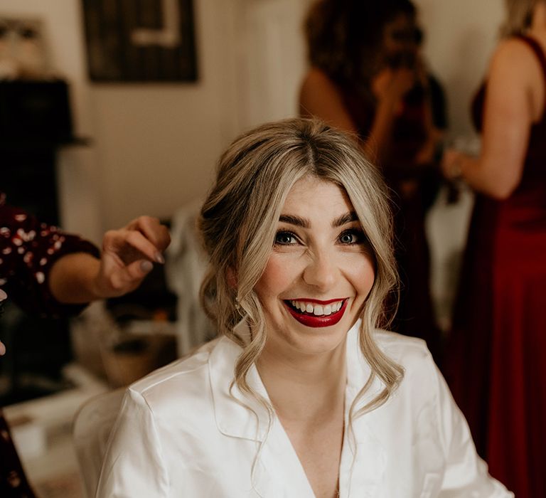 Bride in white satin pyjamas on her wedding morning with bright red lipstick 