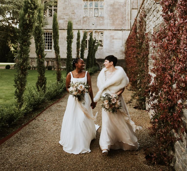 Romantic wedding photographs around Elmore Court with Black bride in a minimalist wedding dress holding hands with her bride in a Anna Kara wedding dress and faux fur stole 