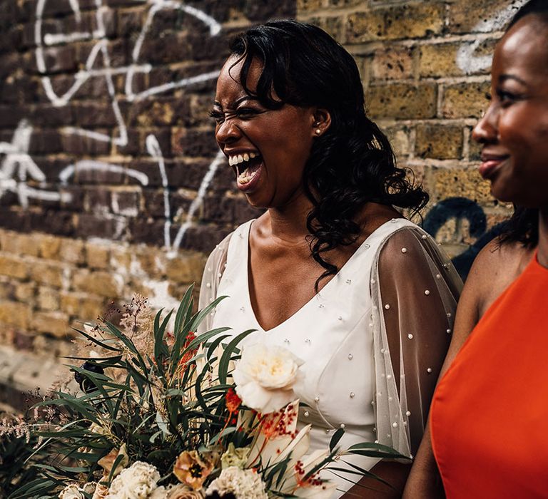 Beautiful black bride in a pearl top laughing with her bridesmaid in a burnt orange dress