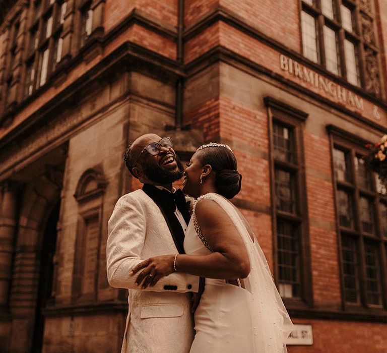 Birmingham city wedding with groom in a white brocade tuxedo jacket laughing with his bride in a Pronovias wedding dress with pearl embroidered Watteau train 