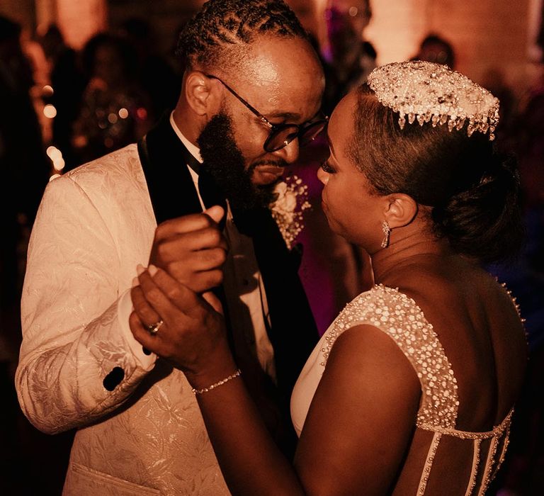 Intimate first dance wedding photograph with bride in a jewel headdresses embracing her husband in a white jacket 