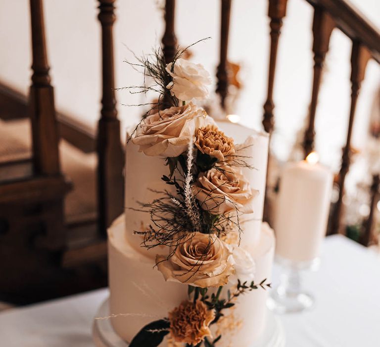 Two tier frosted wedding cake with tofee roses, beige and rust flowers for decoration on white and gold cake stand