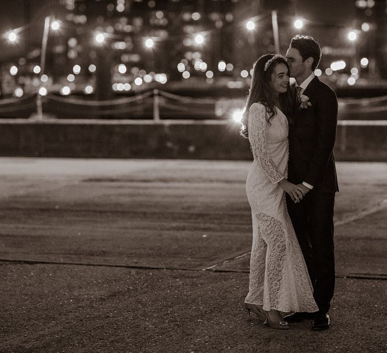 Bride in lace rixo dress with groom looking out at the views of the London city skyline at Trinity Buoy Wharf 