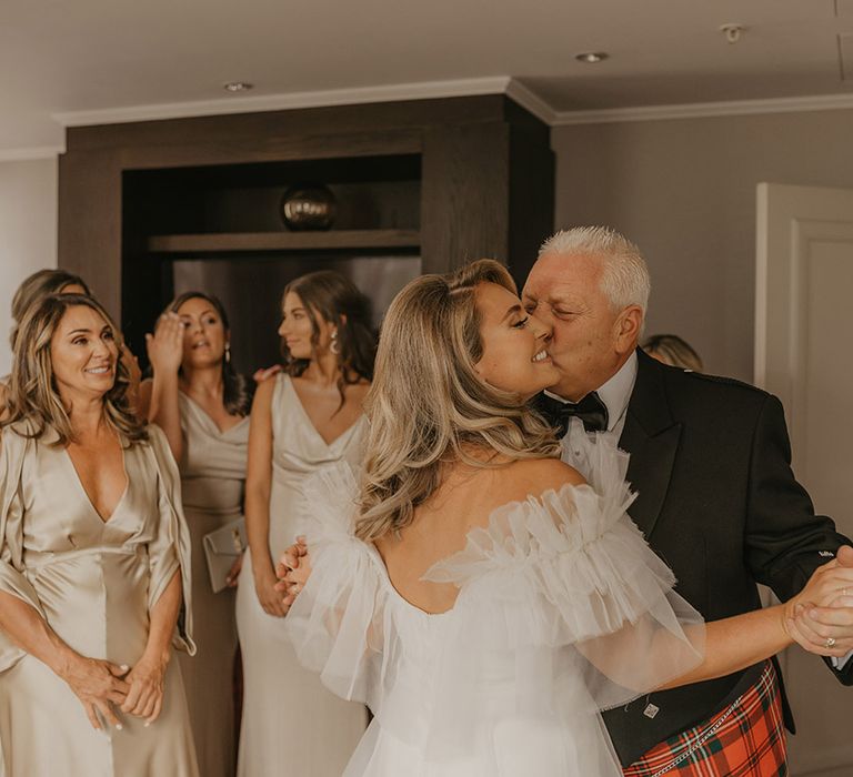 Father of the bride in black tie comes in and kisses the bride on the cheek