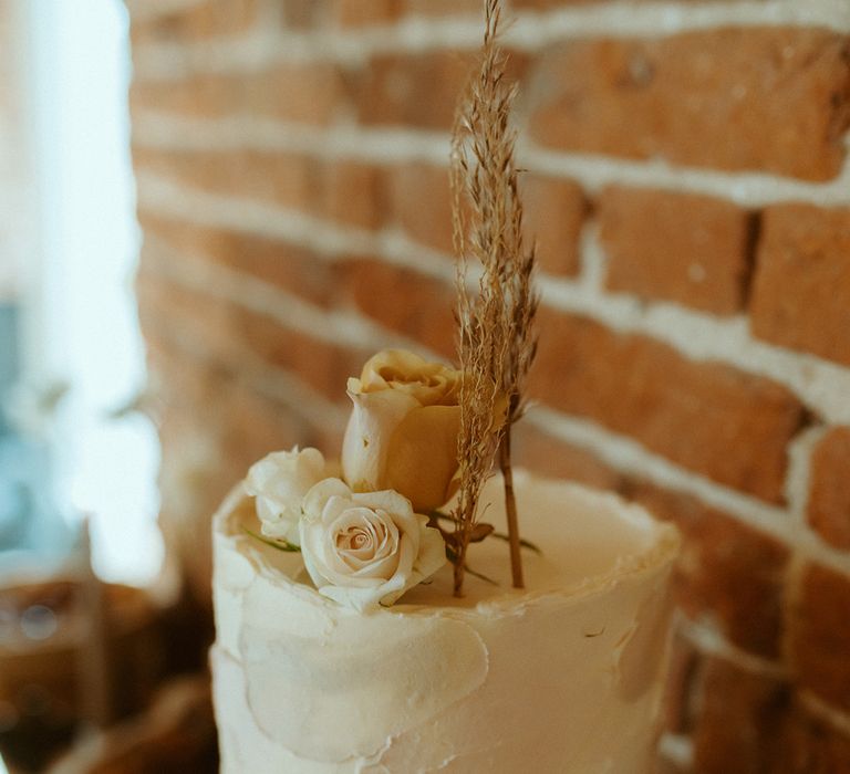 Single tier buttercream wedding cake with white and pink icing topped with flowers and dried wheat