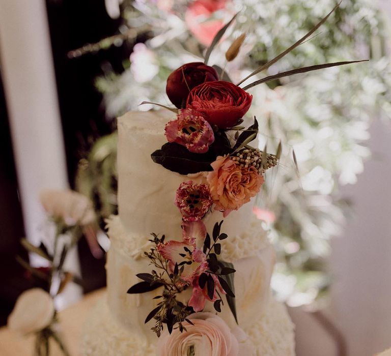 Three tier white frosted wedding cake with icing patterns and decorated with dark flowers