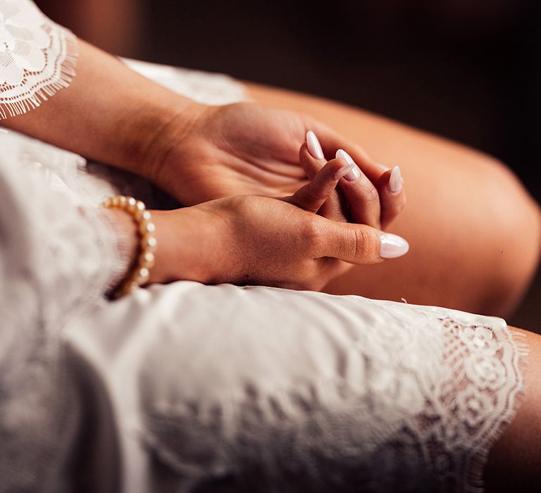 Nude and neutral almond wedding nails for bride wearing pearl bracelet and wearing white robe with lace detail  