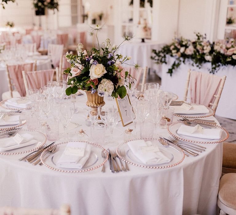 White tablecloths, pink and clear chargers, white rose and colourful flower table centrepiece with chair backs decorated with pink chiffon 