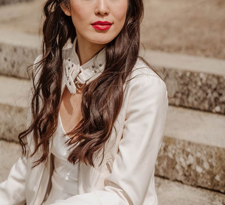 East Asian bride with long wavy hair wearing a flower in har hair, red lipstick and a white leather jacket 