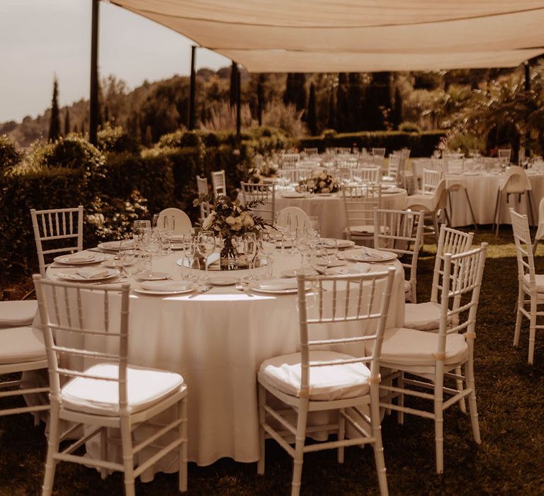 Outdoor wedding reception in Spain complete with round tables and white floral bouquet centrepieces 