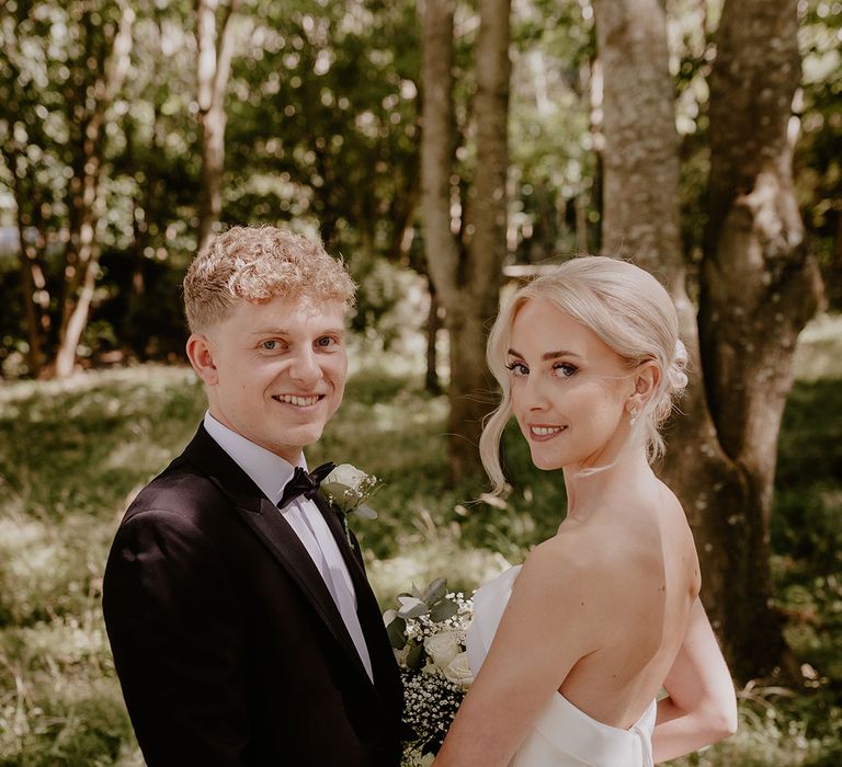 Bride in strapless gown with button detail stands with the groom in black tie