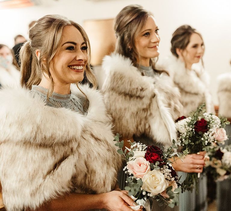 Bridesmaids wear faux fur stoles complete with red and white floral bouquets 