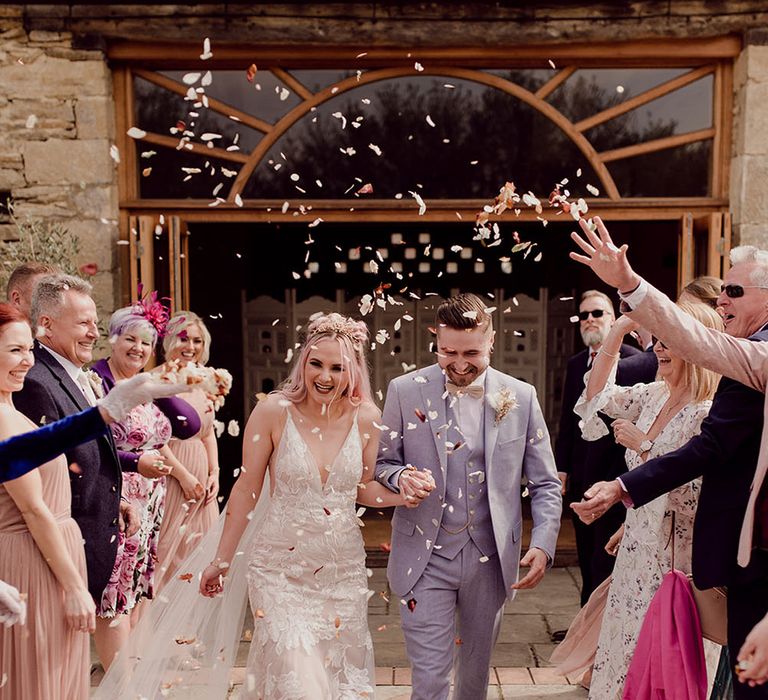 Bride & groom walk through confetti thrown by wedding guests after rustic outdoor ceremony