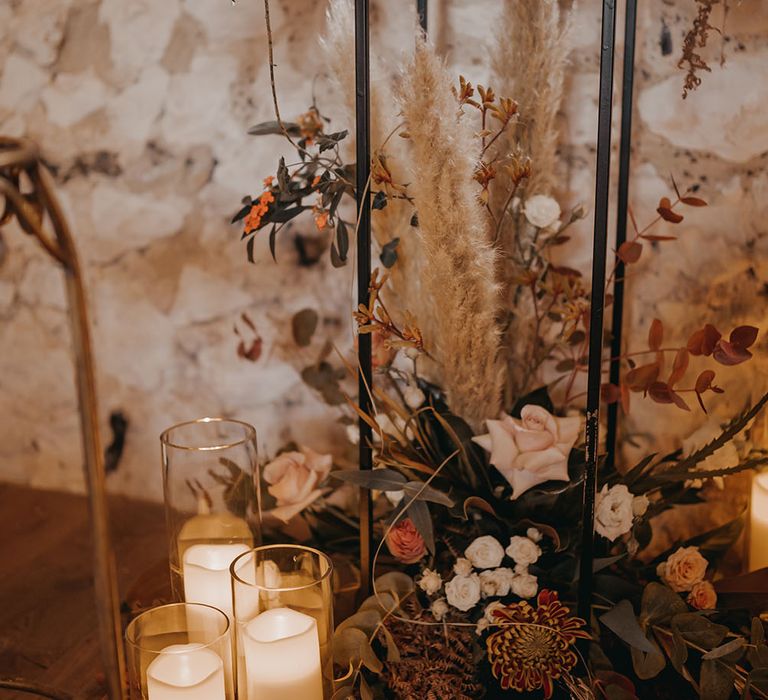 White pillar candles in glass cases surrounded by dried floral arrangements 