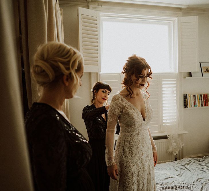 Bride wears lace wedding dress with V-shaped neckline and her red hair in curled half-up half-down styling  