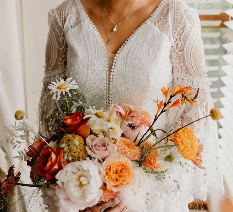 Bride in a boho lace wedding dress with curled blonde updo with a pretty orange, pink and white bouquet 