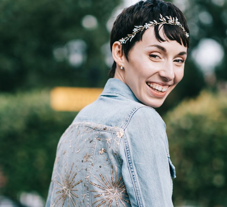 Bride wears her dark hair in pixie cut with bridal crown and wears embellished denim jacket 